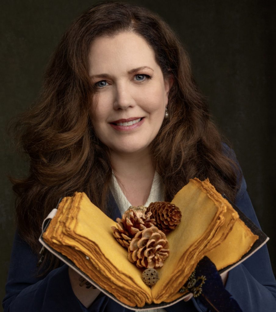 Author Dr. KJ Markeli with an old book and pinecones